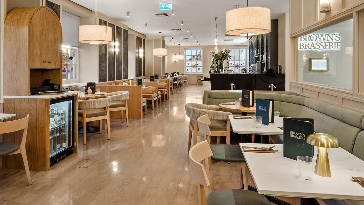 Modern restaurant interior with wooden tables and chairs, large gold lamps, and potted plants.