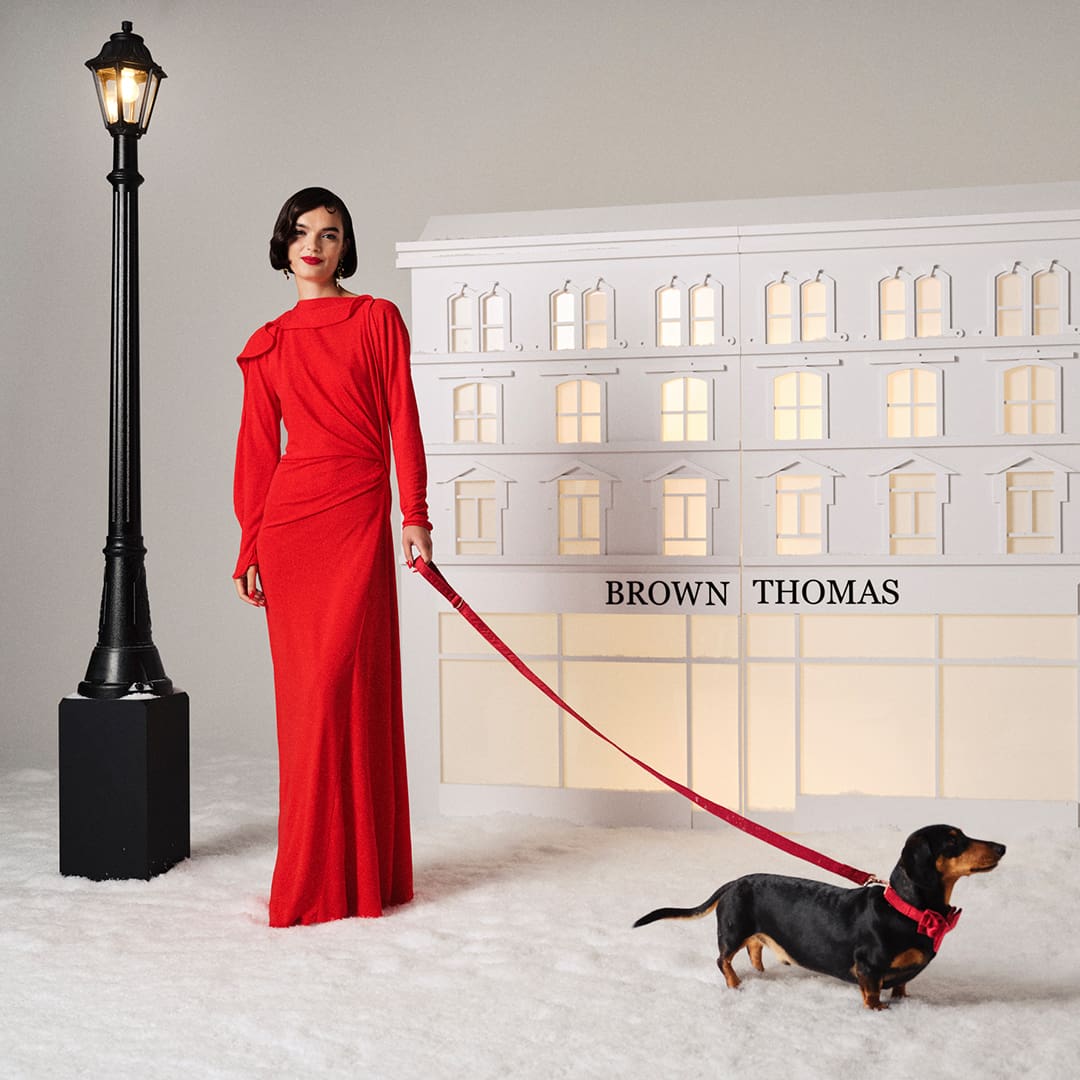 Woman in a red dress holding a small black and brown dog against a red background.